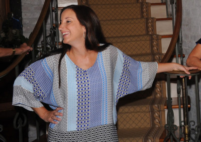 Woman smiling and standing by a staircase, wearing a patterned top and skirt.