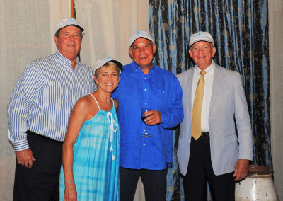 Four adults wearing matching blue hats posing for a photo at a formal event, standing in front of a curtain.