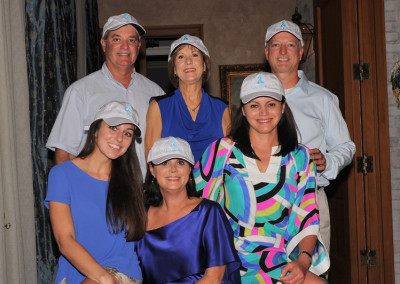 Six people posing for a photo indoors, three women and three men, all smiling and wearing matching blue-themed outfits and visor caps.
