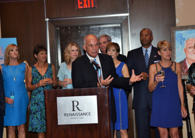 Man speaking at a podium during an event at the renaissance venue while a group listens, some holding drinks.