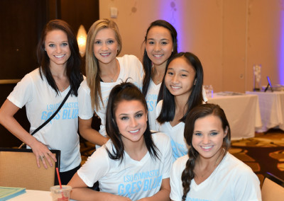 Six women in matching "lisanti gresi blue" t-shirts smiling at a conference table in a ballroom.