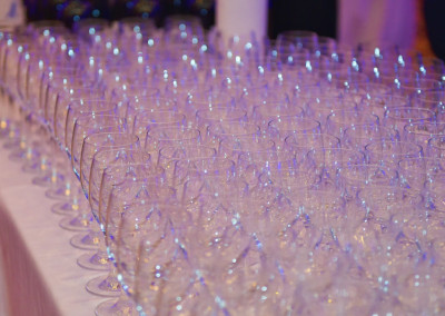 Rows of empty wine glasses arranged on a table, illuminated by soft blue lighting.