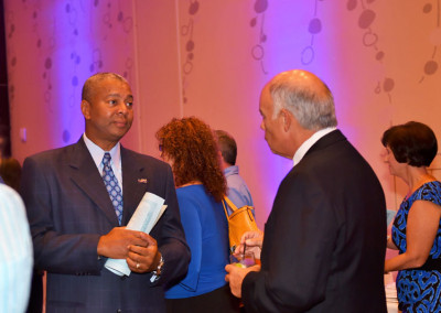 Two men in business attire conversing at a networking event, with other attendees in the background.