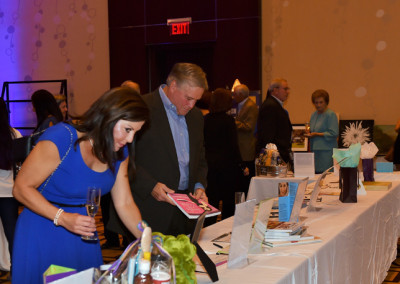 People browsing items at a charity auction event in a hotel ballroom.