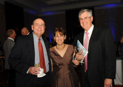 Three adults at a formal event, standing together smiling, two men and a woman holding an award.