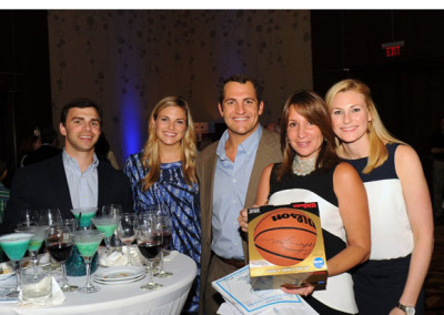 Five people smiling at a banquet table with drinks, one holding a basketball and another holding a certificate.