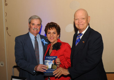 Three individuals (two men and one woman) posing with a book titled "cancer" at an event. the woman is holding the book, and all are smiling.