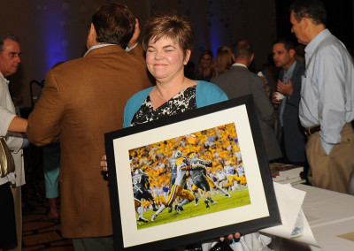 A woman smiling while holding a framed sports photograph at a crowded event.