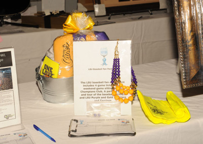 Auction table display featuring lsu baseball fan package with game tickets, purple and gold beads, and a cap.