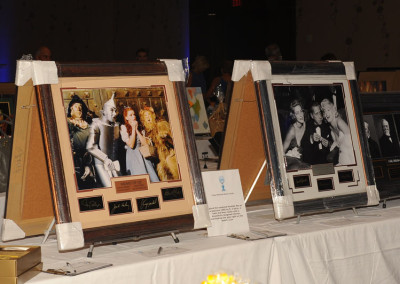 Framed celebrity photographs displayed on easels at an auction event with descriptions and plaques.