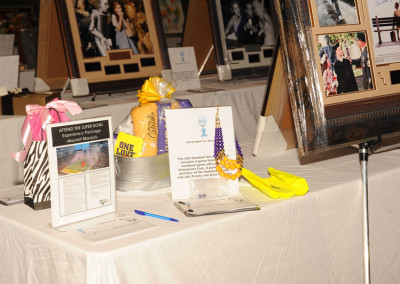 An exhibition table with event flyers, framed photographs, and gift bags displayed.