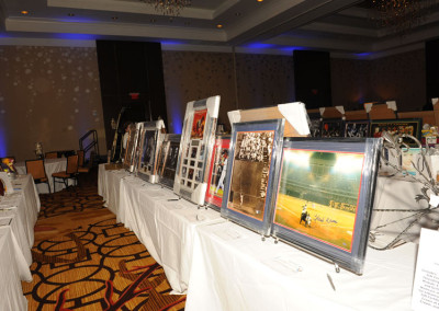 Row of framed sports photographs displayed on a table at a charity auction event in a hotel banquet hall.