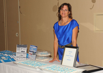 A woman in a blue top stands behind a table with informational brochures and cookies at an event.
