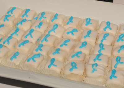 A tray of white-frosted petit fours decorated with blue ribbons, likely symbolizing support for prostate cancer awareness.