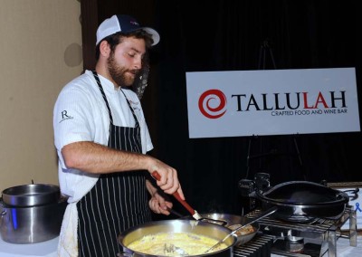A chef cooks in a pan at a booth with "tallulah crafted food and wine bar" signage in the background.
