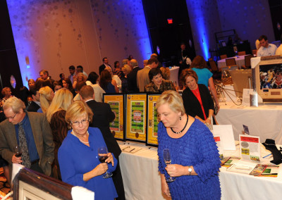 People at a social event in a ballroom, looking at displays, some holding drinks.