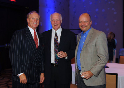 Three smiling men in business attire standing together at a formal event.