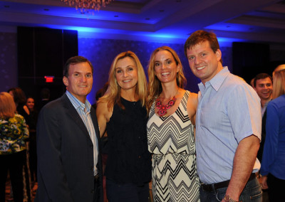 Two couples posing happily at an indoor event with a blue-lit background.