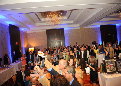 People attending a formal event in a hotel ballroom with chandeliers, some are taking photos.