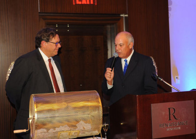 Two men conversing at a podium with a "renaissance" sign, one holding a microphone in a formal setting.