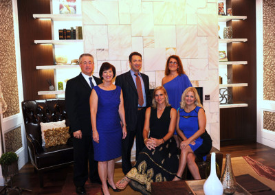 Six adults posing for a photo in a stylish room with a marble wall and shelving displaying various items.
