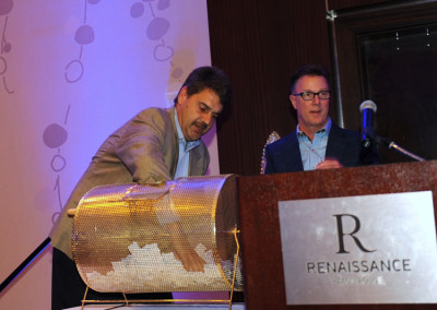 Two men at a podium, one turning a raffle drum, at a renaissance hotel event.