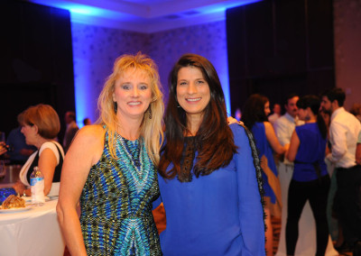 Two women smiling at a social event in a room with blue lighting.