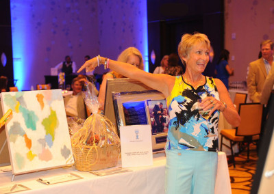 A woman in a patterned top smiling and pointing to an auction item at a charity event.