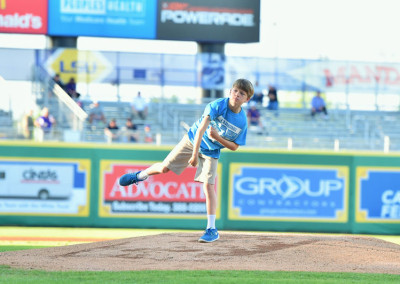 A young boy pitching a baseball on a sunny day at a sports stadium.