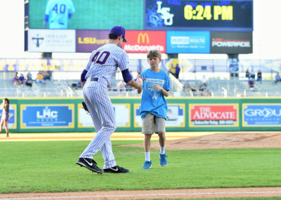 A young fan shakes hands with a baseball player on the field, with a scoreboard showing the time at 6:24 pm in the background.