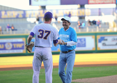 Baseball player in purple uniform numbered 37 shakes hands with a smiling man in a blue shirt on a baseball field.
