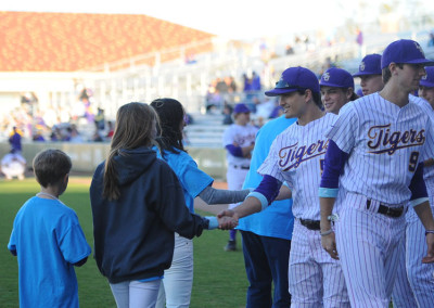 Young fans shaking hands with baseball players in striped uniforms on a field, with spectators in the background.