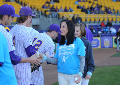 A woman and a young girl in blue shirts shaking hands with baseball players in purple uniforms on a field.