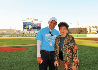 An older couple smiling on a baseball field at lsu's alex box stadium, with the scoreboard in the background.