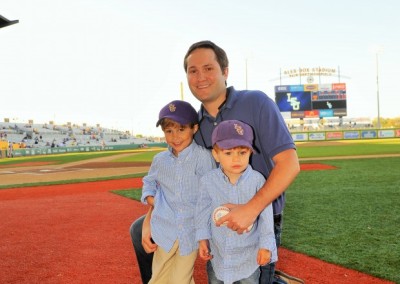 A man and two young boys wearing baseball caps smile for a photo on a baseball field.