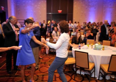 A group of people dancing in a room with tables and chairs.