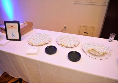 Table at an event displaying plates of blue and white frosted cupcakes arranged in rows, with a framed sign and napkins on the side.