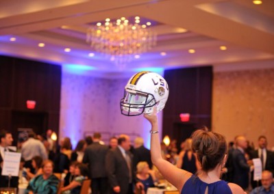 Woman holding an lsu football helmet up in a crowded banquet hall.