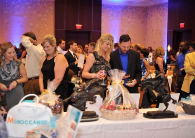 People browsing items at a charity auction event, with various baskets and sculptures on display.