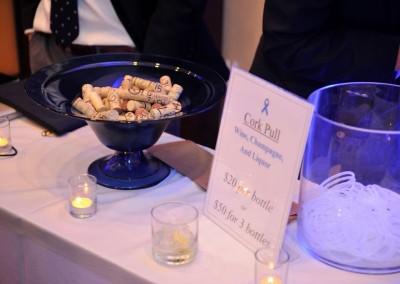 A bowl filled with wine corks beside a sign for a cork pull fundraising event, with prices listed and candles nearby.
