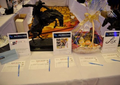 Silent auction display featuring a bronze horse statue, gift baskets, and bid sheets on a table at a charity event.