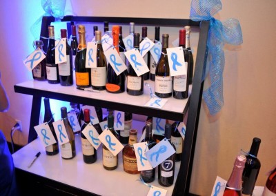 A display of various wine bottles adorned with blue ribbons on a shelf at an event.