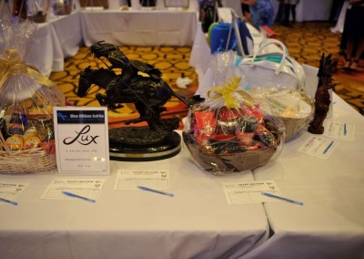 Table displaying various auction items including gift baskets and a black sculpture, with bid sheets in front at an event.