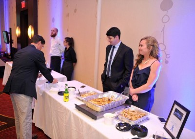 People at a buffet line with a man serving himself, another chatting, and a woman smiling, in a banquet hall.