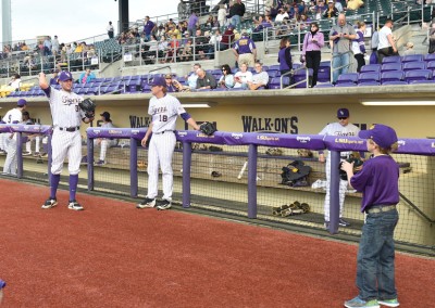Young boy with a camera photographing baseball players in purple uniforms at a stadium.