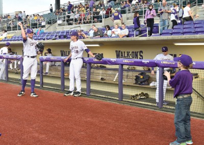 A young boy extends a baseball for an autograph to a player in the dugout, while other players watch during a baseball game.