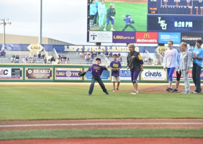 A child in a baseball uniform throws the first pitch at an lsu baseball game as spectators watch.