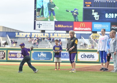 A young boy throws a ceremonial first pitch at an lsu baseball game, watched by spectators and a mascot on the field.