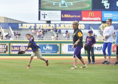 Young boy in purple jersey catching a baseball in a stadium, with spectators and players watching.