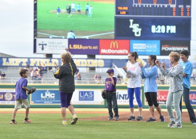 A group of people, including children, participating in an on-field activity at an lsu baseball game.